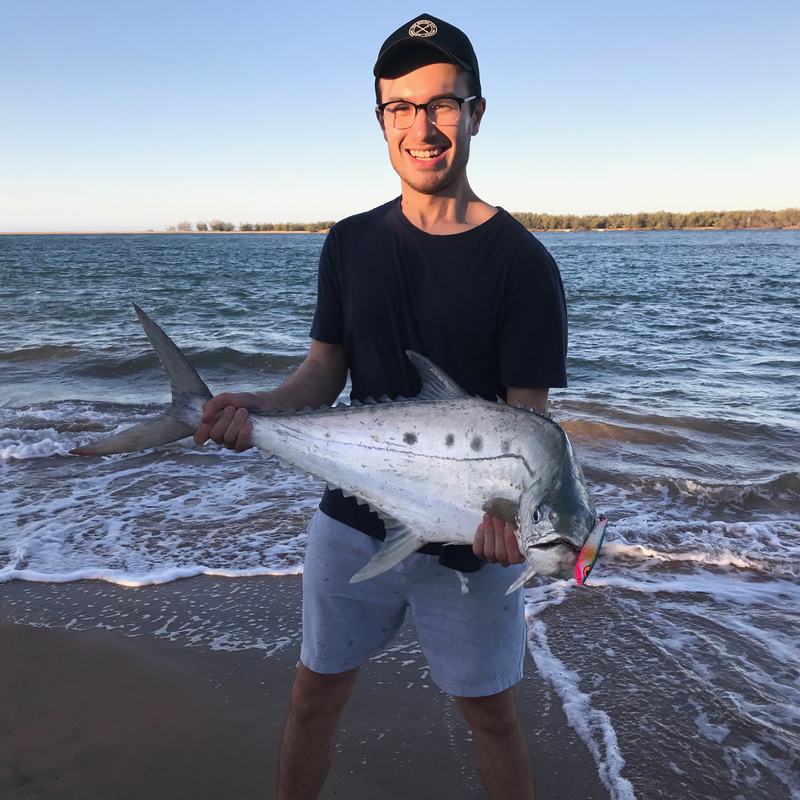 A smiling angler stands in the shallows holding a large silver fish.